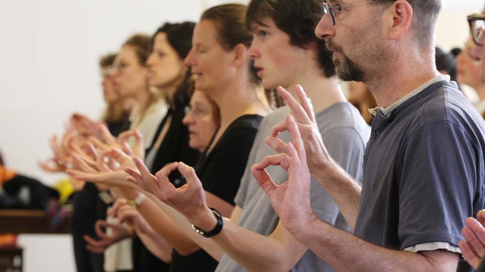 Männer und Frauen stehen in einer Reihe und formen ihre Hände und Finger zur Gebärdensprache