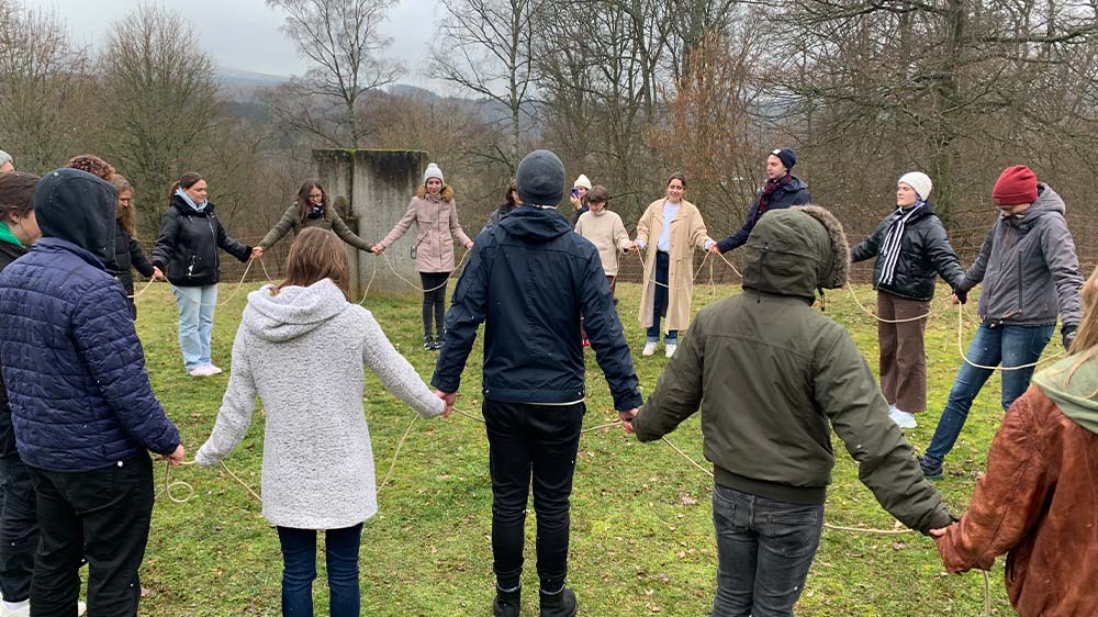 Junge Menschen stehen auf dem Gras draußen und halten sich und ein Seil an den Händen