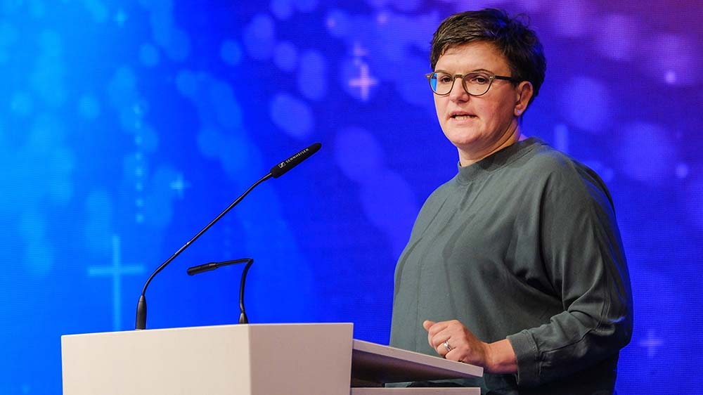 Frau mit Brille und Pullover an einem Rednerpult