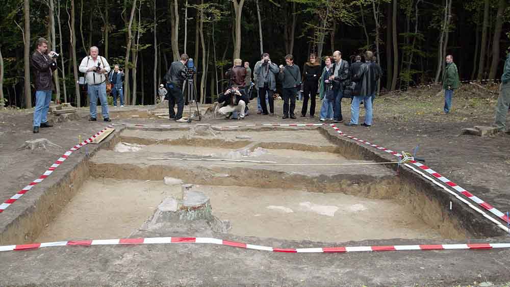 Vor einem ausgebuddelten Loch stehen mehrere Leute mit Kameras und Fotoapparaten