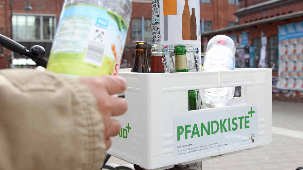 Eine Frau deponiert in Hamburg eine Pfandflasche in einer Pfandkiste der Aktion "Pfand gehört daneben"