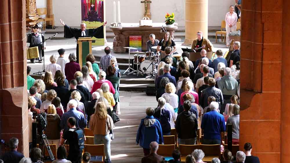 In einer voll besetzten Kirche breitet der Pastor die Arme zum Segen