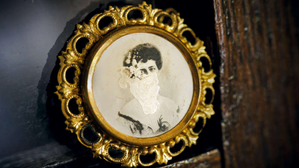 Das Bild einer Frau, eingeklebt in eine goldene Brosche, ist beschädigt und nicht mehr zu erkennen