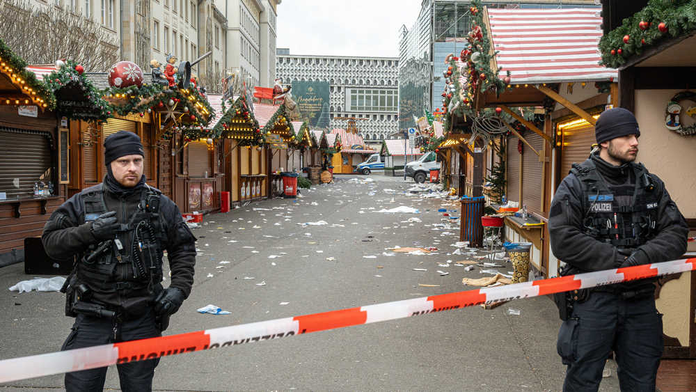 Zwei Polizisten stehen vor einem leeren Weihnachtsmarkt, der mit Flatterband abgesperrt ist