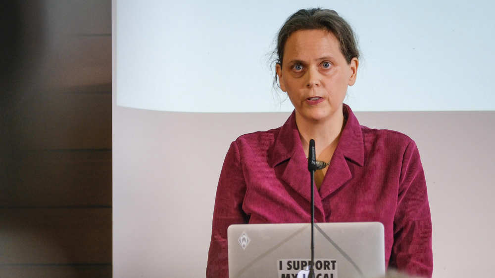 Junge Frau mit pinker Bluse steht mit Laptop auf einem Rednerpult