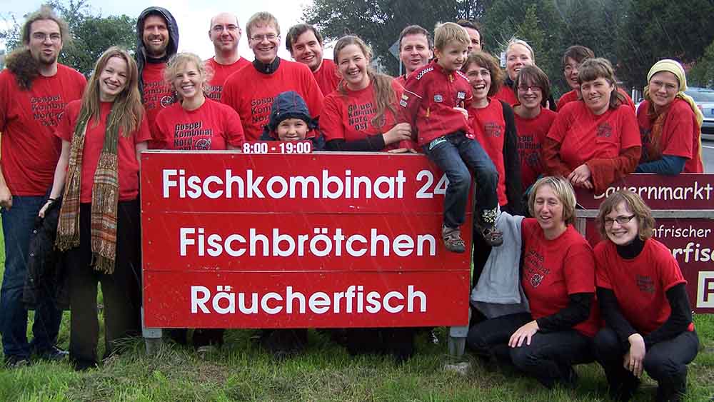 Viele Menschen in roten Shirts stehen um ein Schild mit der Aufschrift Fischkombinat