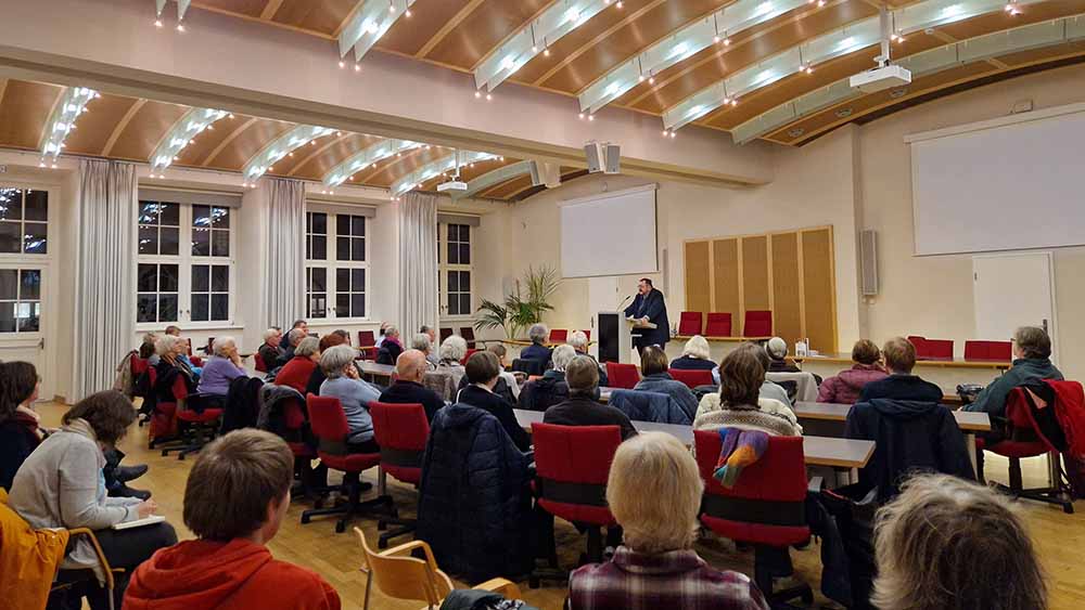 Saal mit vielen Zuhörenden, ein Redner steht vorn am Pult