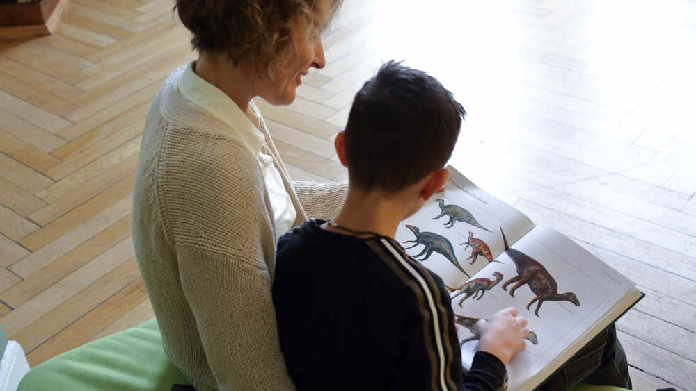 Frau liest mit Kind in einem Dino-Buch