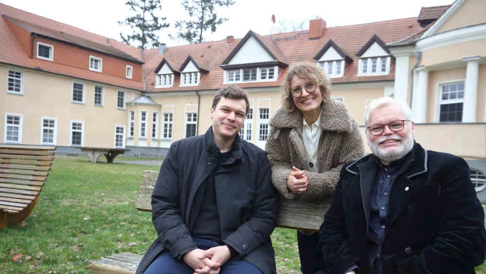 Drei Erwachsene sitzen auf Bank im Innenhof
