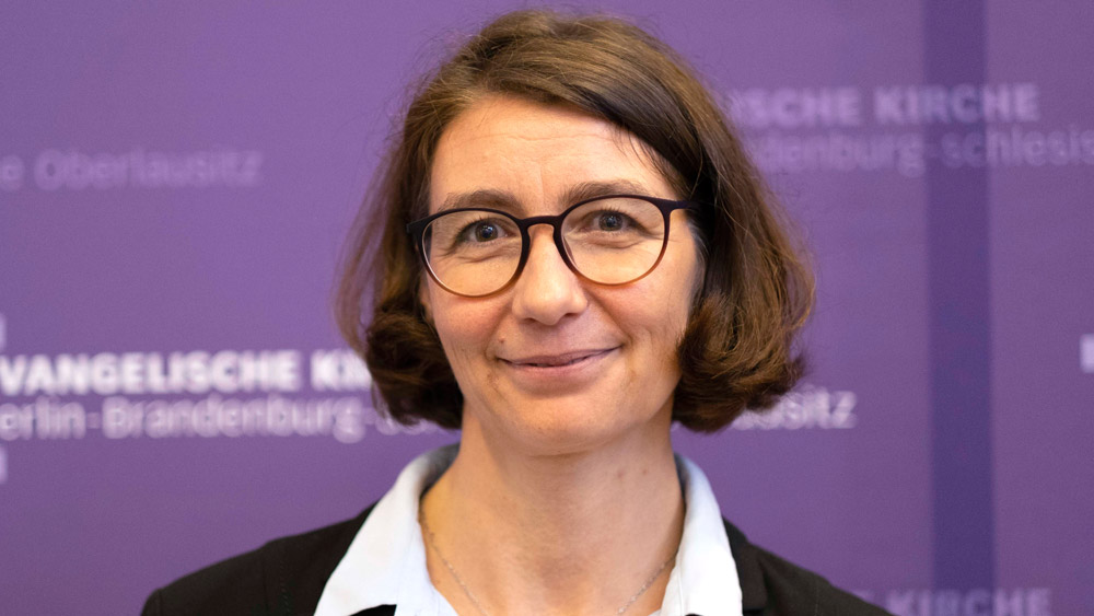 Lächelnde Frau mit Brille vor lilafarbenem Hintergrund