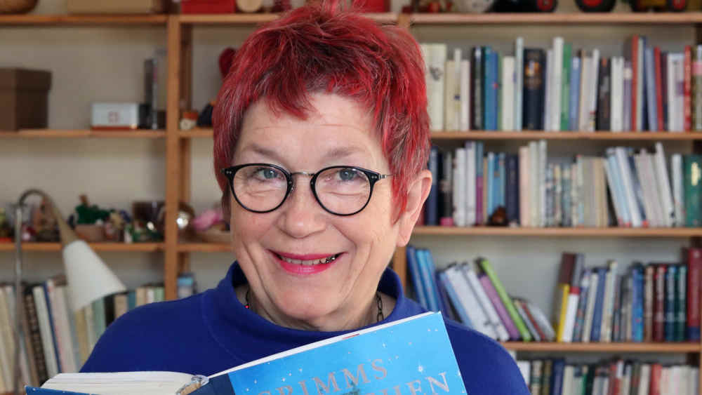 Frau mit kurzen roten Haaren hält Grimms Märchenbuch in den Händen