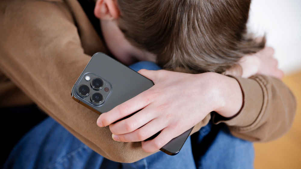 Junge mit Handy in der Hand kauert am Boden