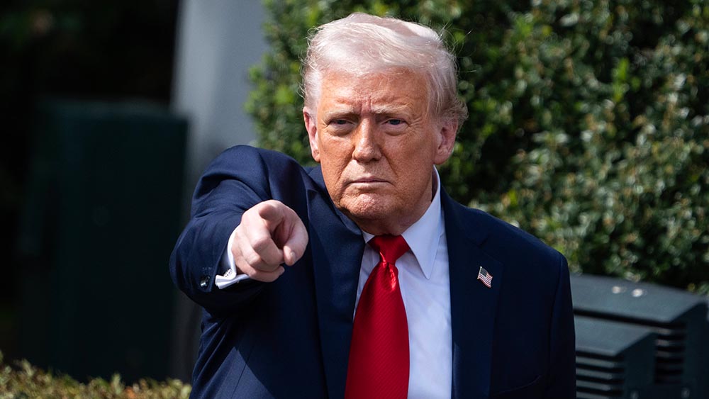 Mann im Anzug mit roter Krawatte und blonden Haaren zeigt mit Finger auf Kamera