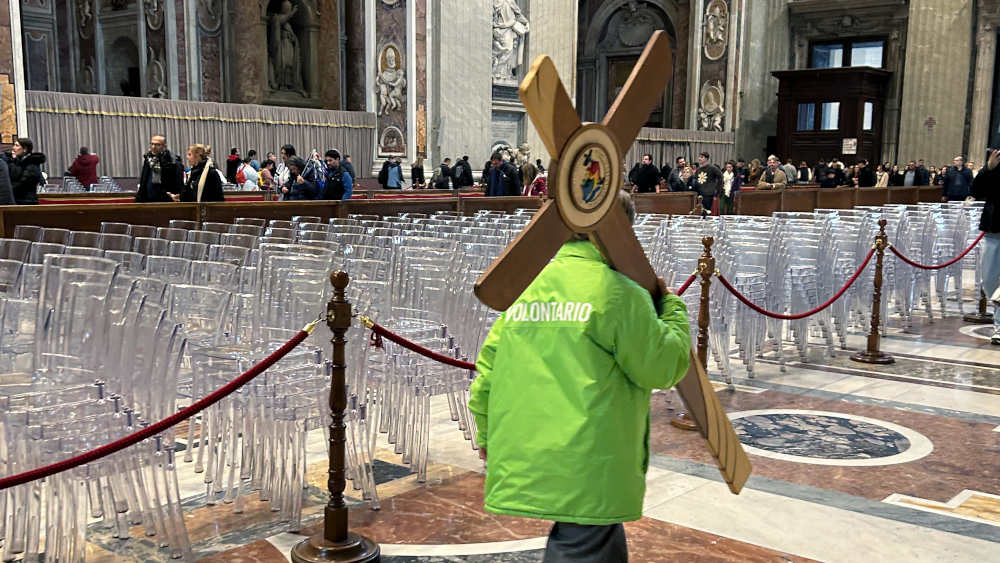 Mann in hellgrüner Jacke trägt ein Holzkreuz