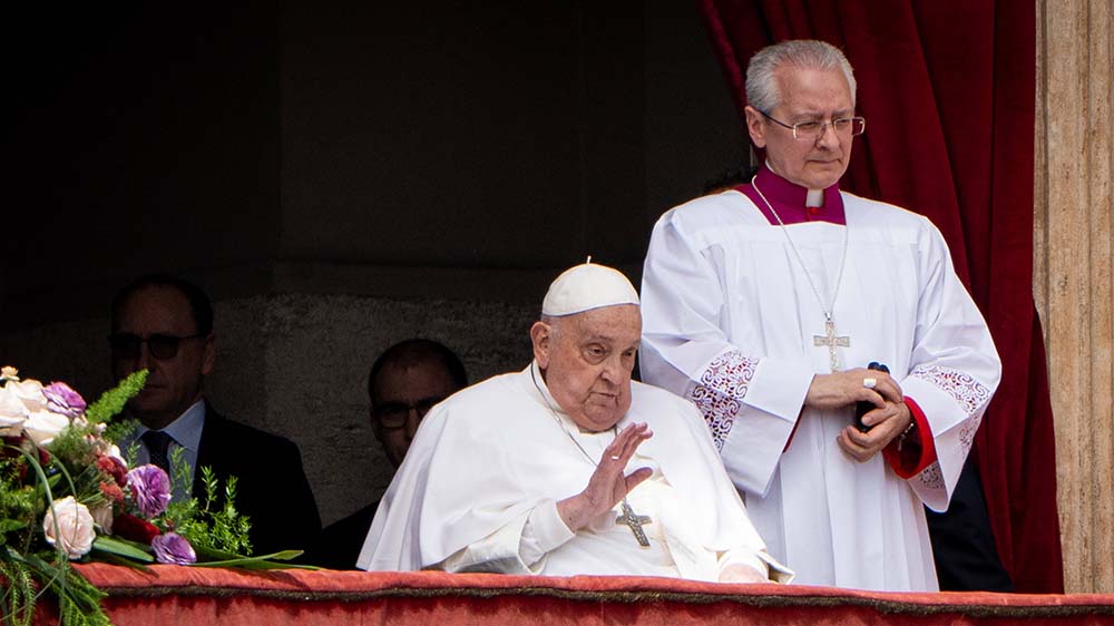 Mann im weißen Gewand sitzt an einem Balkon, weiterer Mann steht hinter ihm