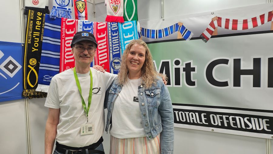 Ein Mann und eine Frau stehen vor Fanschals von verschiedenen Fußballvereinen.