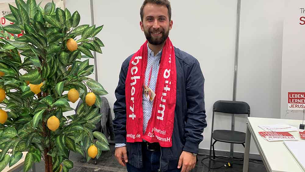 Mann mit rotem Schal steht neben einem Orangenbaum