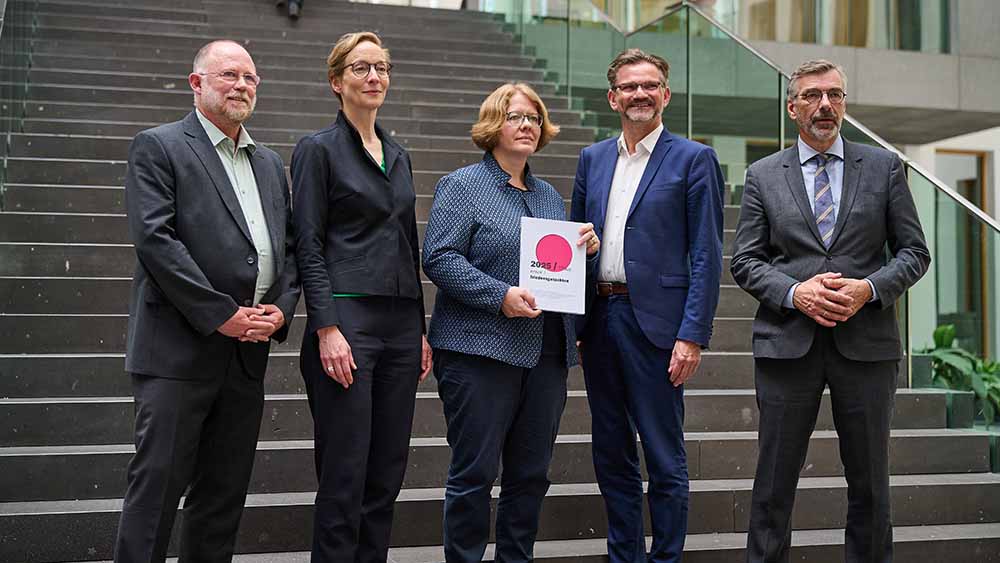 Fünf Menschen stehen auf einer Treppe. Eine Frau in der Mitte hält ein Buch auf Hüfthöhe.