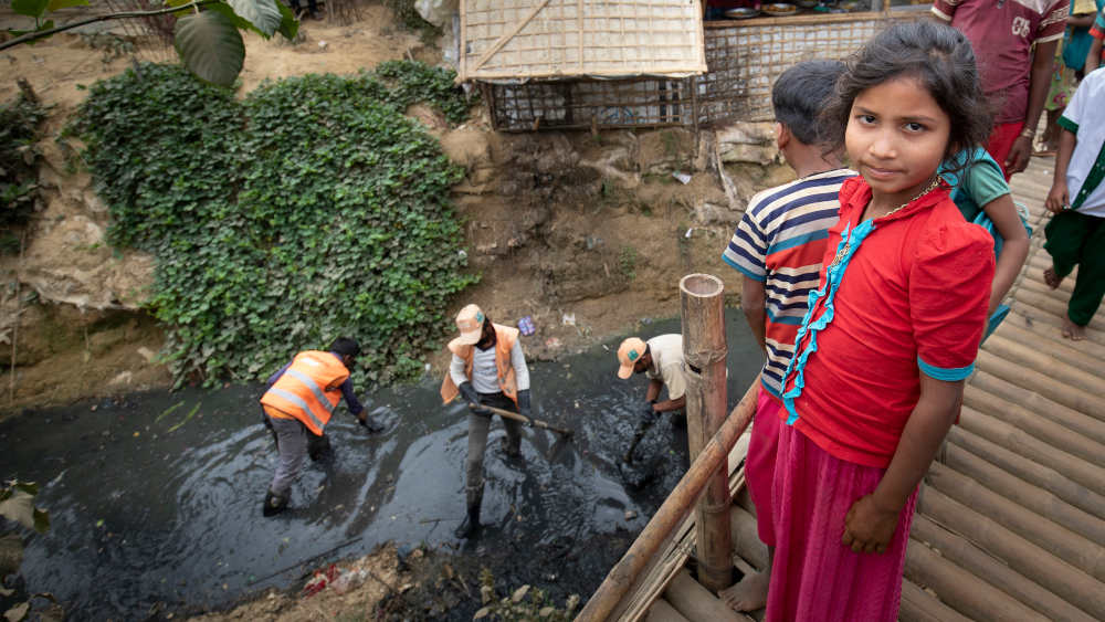 Mädchen vor schwarzer Kloake, in der Männer arbeiten