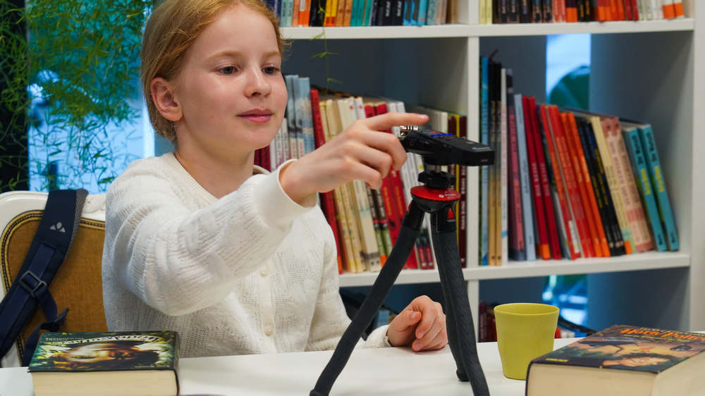 Mädchen im weißen Pullover sitzt an einem Tisch vor einem Mikfrofon