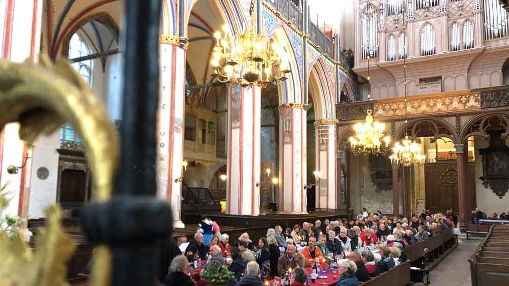 Blick in einen Kirchenraum mit reich verzierten hohen Säulen, Rippengewölbe, Orgel und mehr.