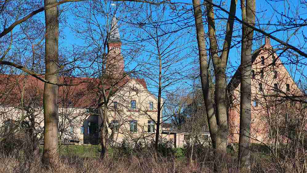 Blick auf eine Gebäudeanlage mit einer Kirche dahinter. Der Kirchturm ist zu sehen.