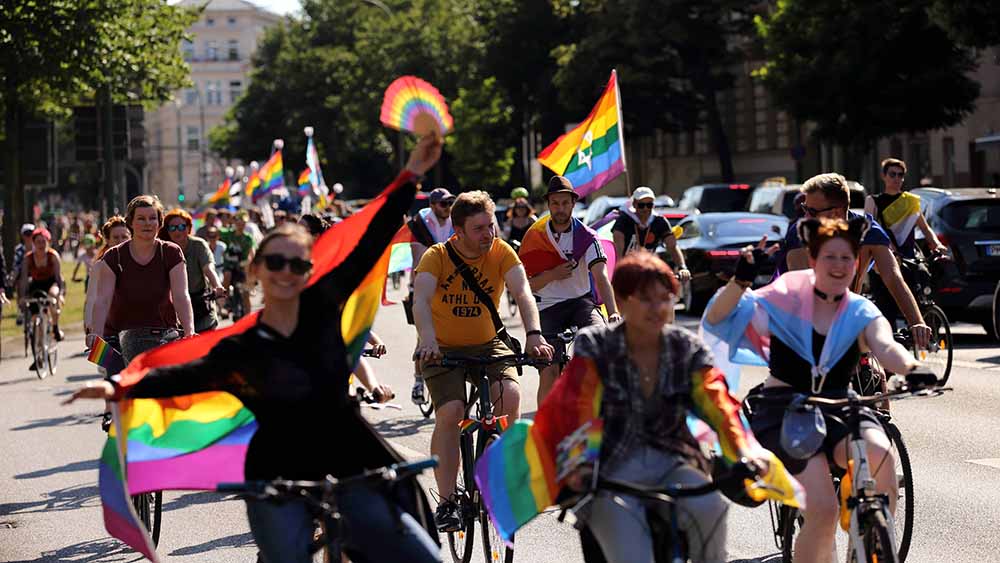 Menschen fahren Fahrrad und haben bunte Flaggen in der Hand oder auf den Schultern liegen