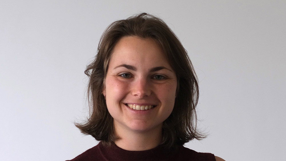 Eine junge Frau lächelt in die Kamera. Sie hat dunkle, schulterlange Haare und trägt ein schwarzes Shirt.