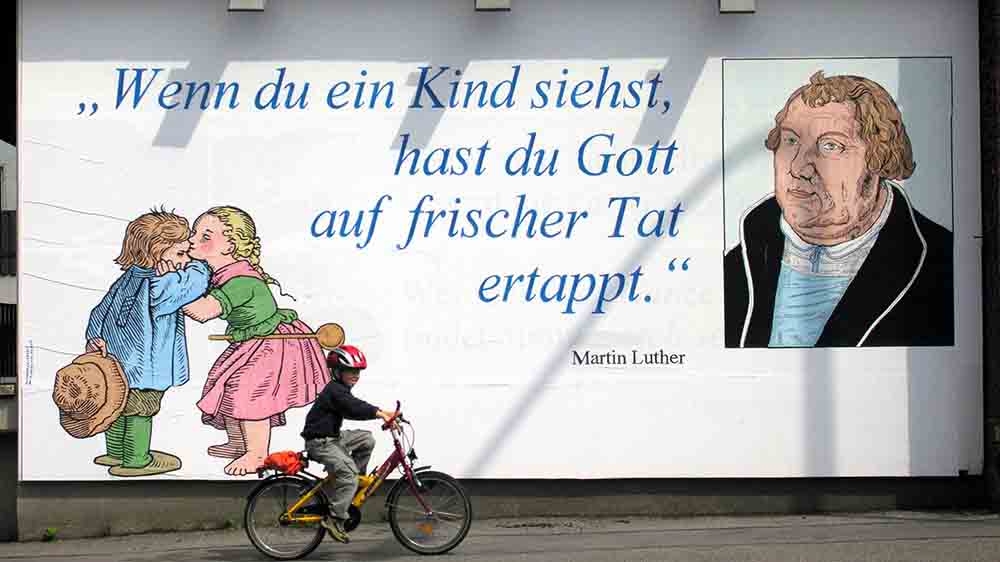 Kind auf Fahrrad fährt an großem Plakat vorbei