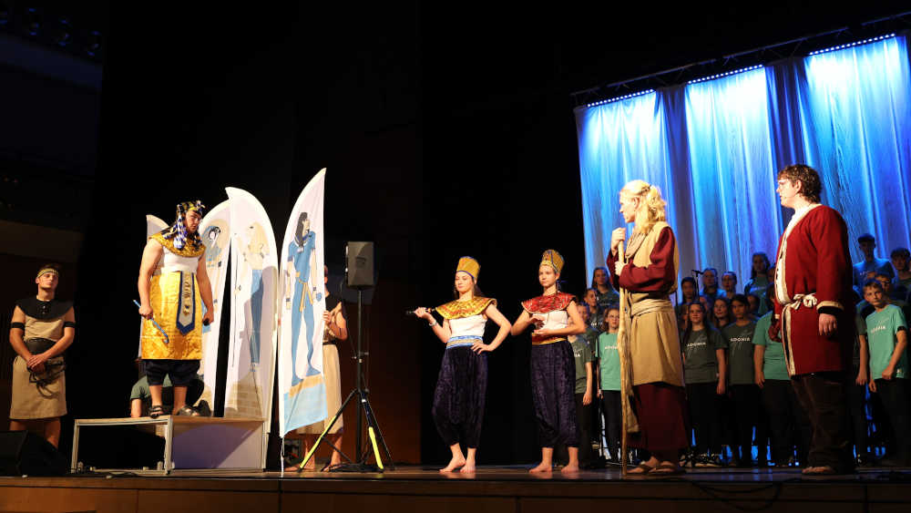 Junge Schauspieler auf der Bühne, im Hintergrund ein Kinderchor