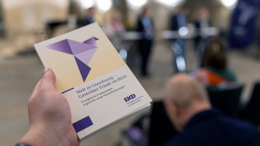 Buch vor einem Podium mit mehreren Leuten