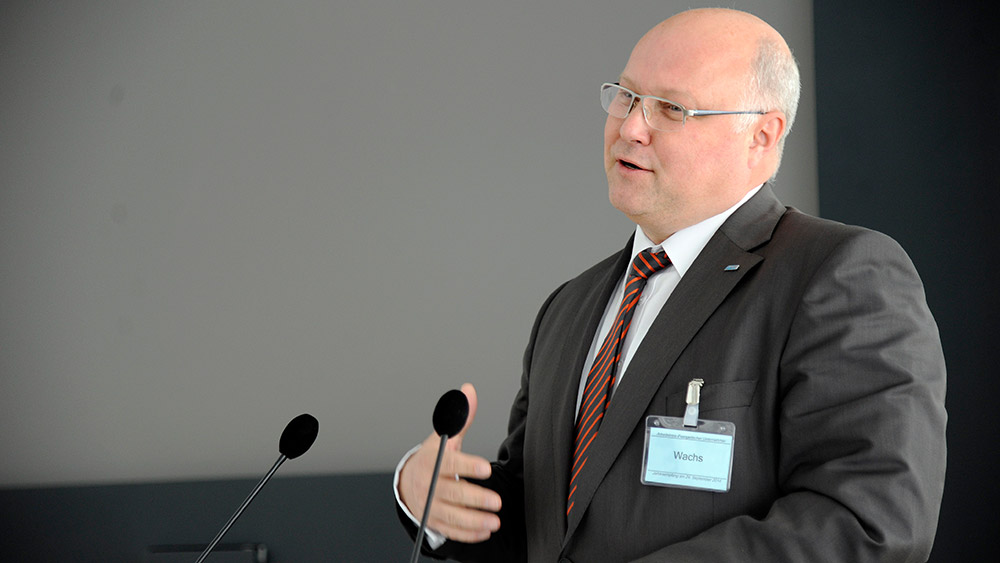 Mann im dunklen Anzug und roter Krawatte mit Glatze steht an einem Rednerpult und spricht