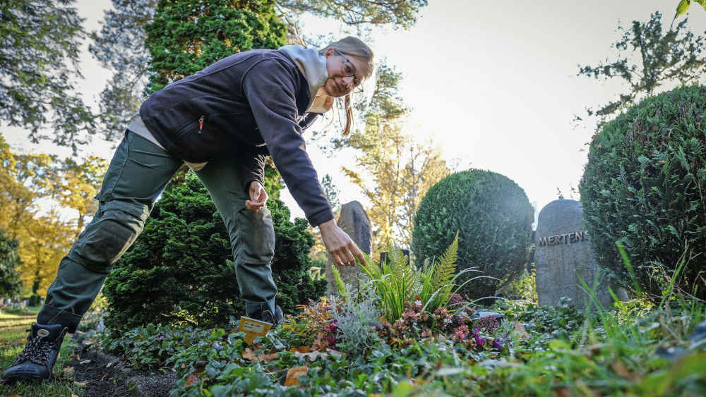 Junge Frau beugt sich über eine Grabstelle