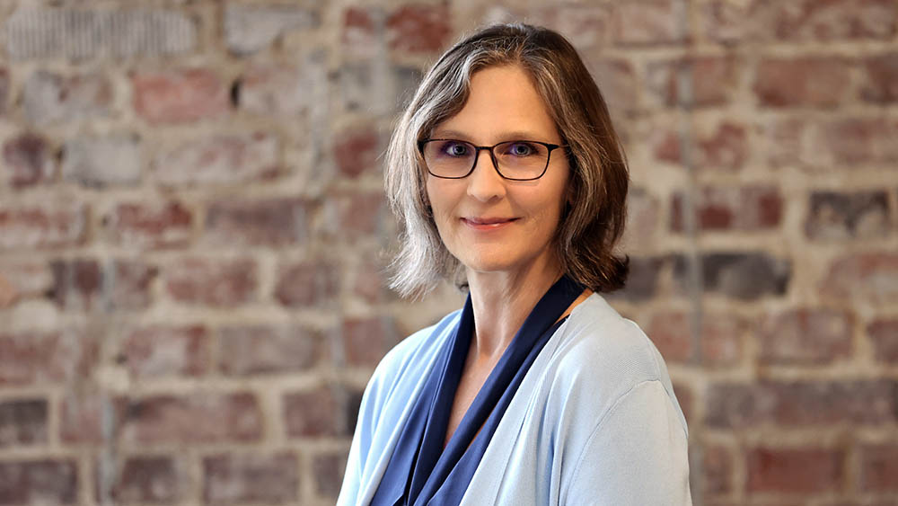 Frau mit schwarzer Brille und hellblauer Bluse schaut in die Kamera