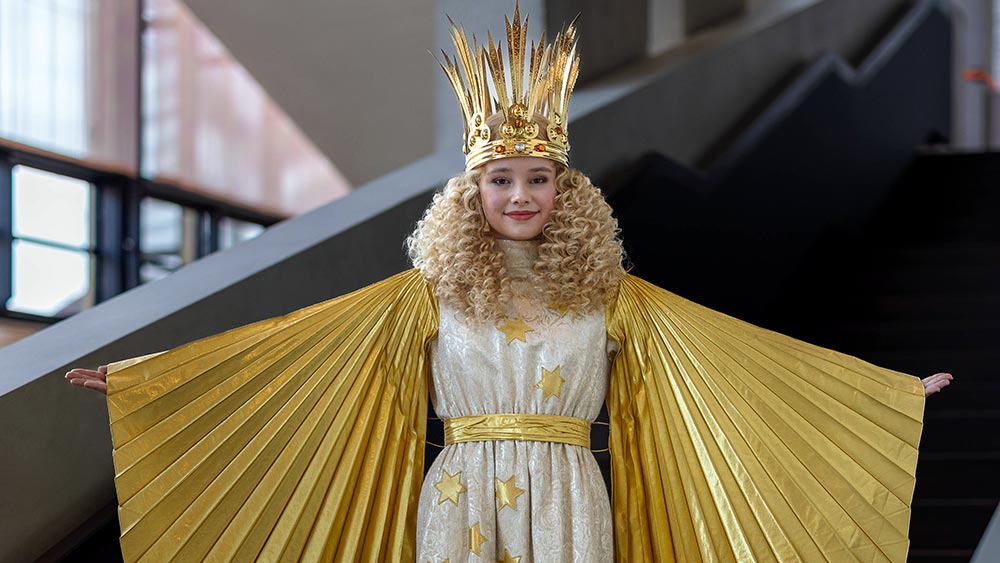Kind in einem goldenem Kostüm mit Krone steht auf einer Treppe