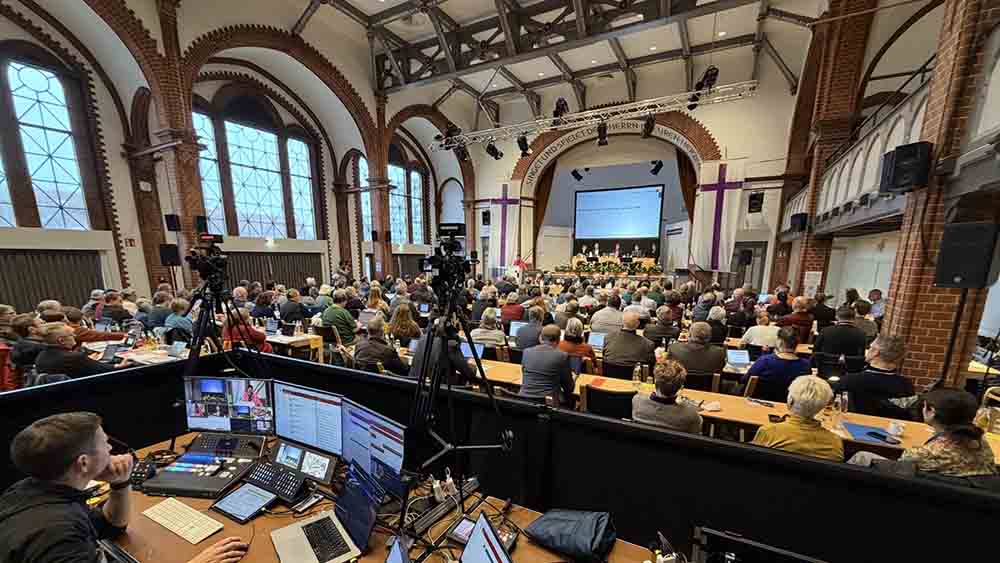 Großer Saal mit Technikpult und vielen Menschen an Tischen.