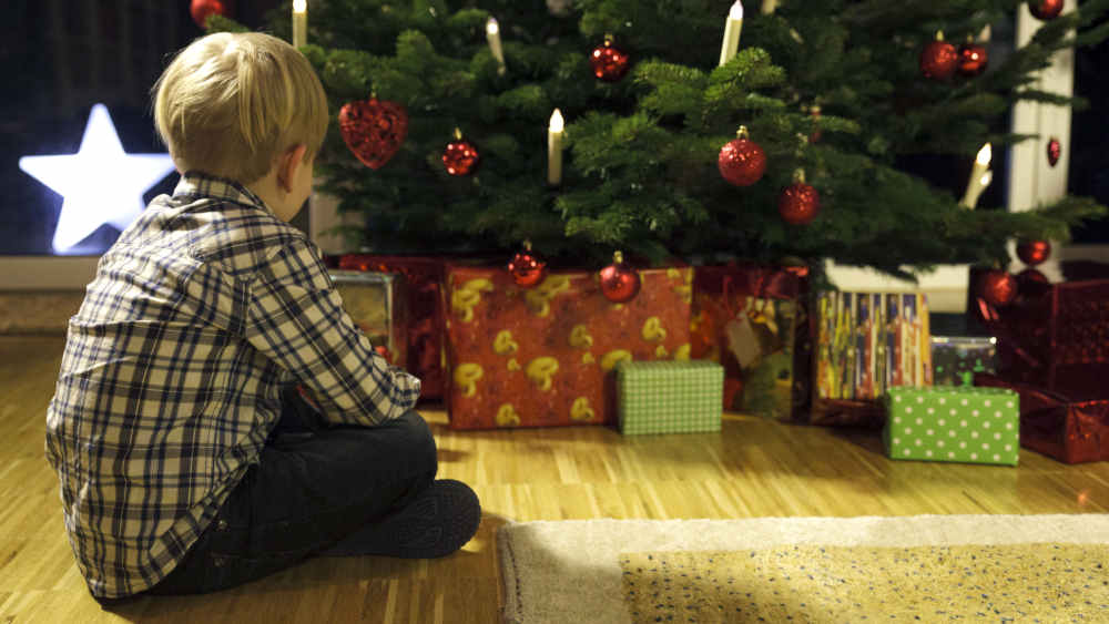 Junge sitzt vor seinen Geschenken am Weihnachtsbaum