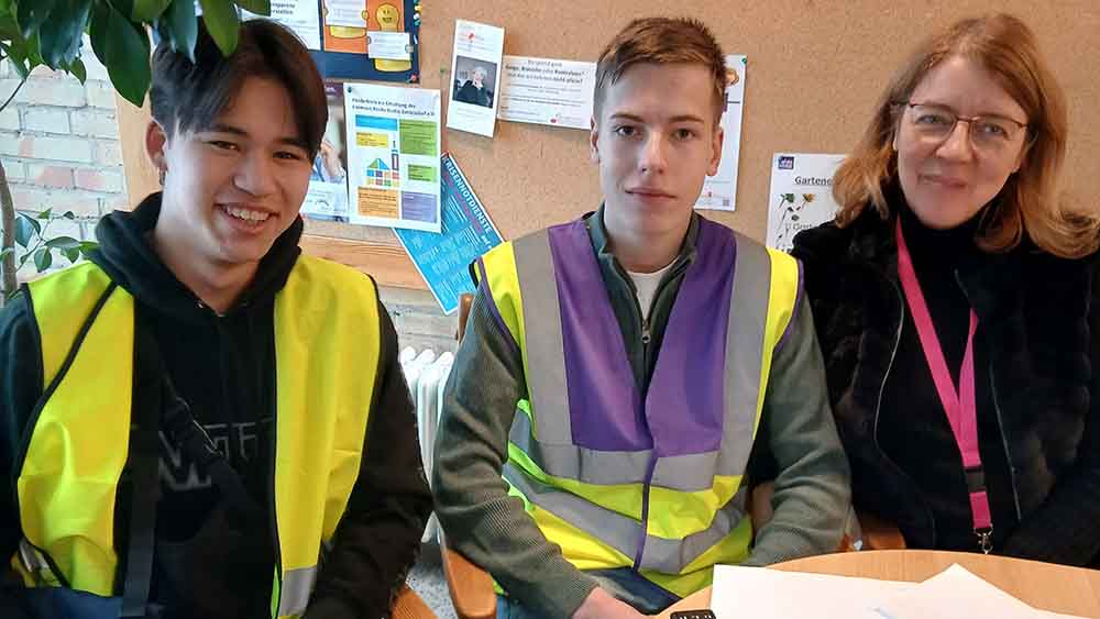 Drei Personen sitzen an einem Tisch, auf dem weiße Blätter liegen.