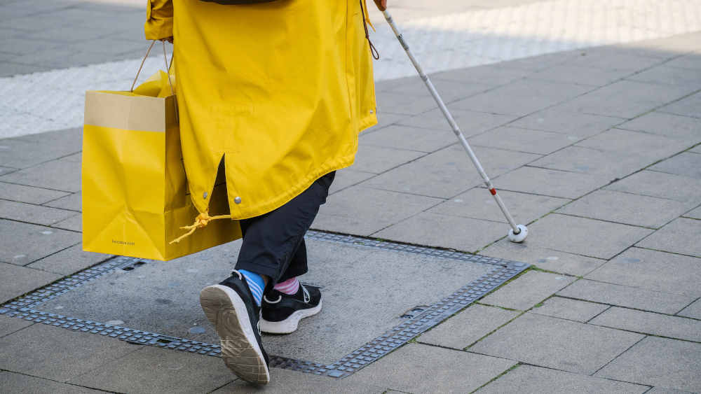 Frau mit gelben Mantel läuft mit Blindenstock