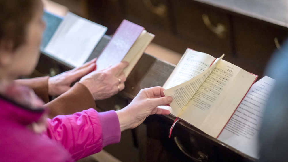 Personen blättern in Gesangbuch auf Kirchenbank