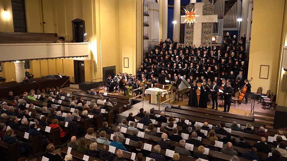 Eine gefüllte Kirchen mit einem Chor, der im Altarraum steht. Die Kirche ist hell beleuchtet.