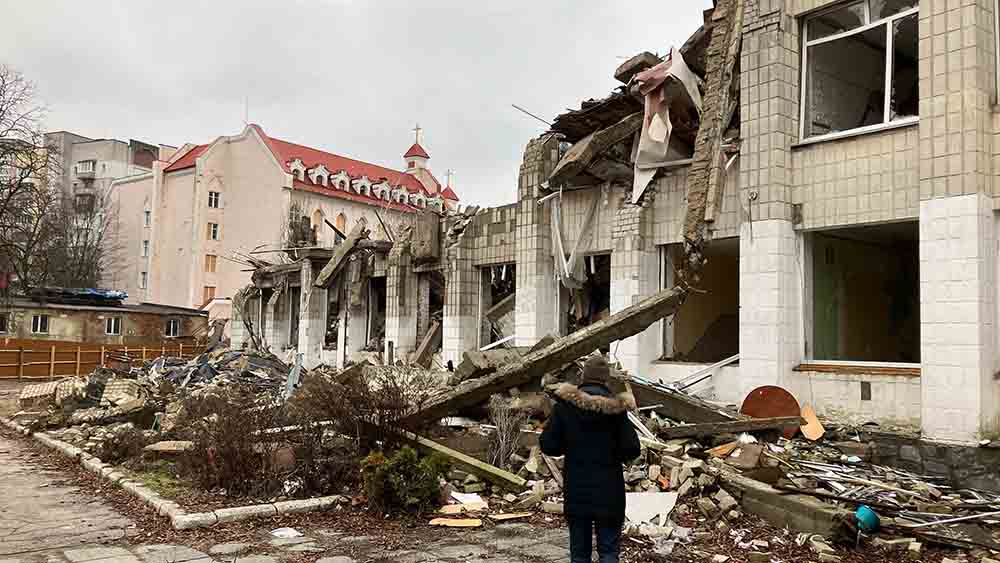 Eine Schule in Trümmern. Ein Mensch steht davor und sieht hoch.