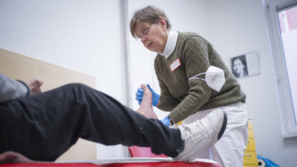 Allgemeinmedizinerin behandelt einen Patienten am Fuß