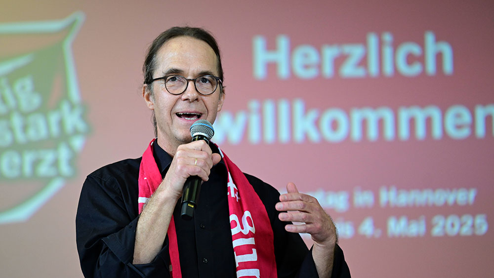 Mann mit rotem Schal und schwarzem Hemd spricht auf Bühne in Mikro