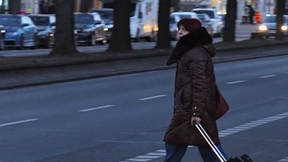 Eine Frau mit dunkler Jacke läuft über eine Straße