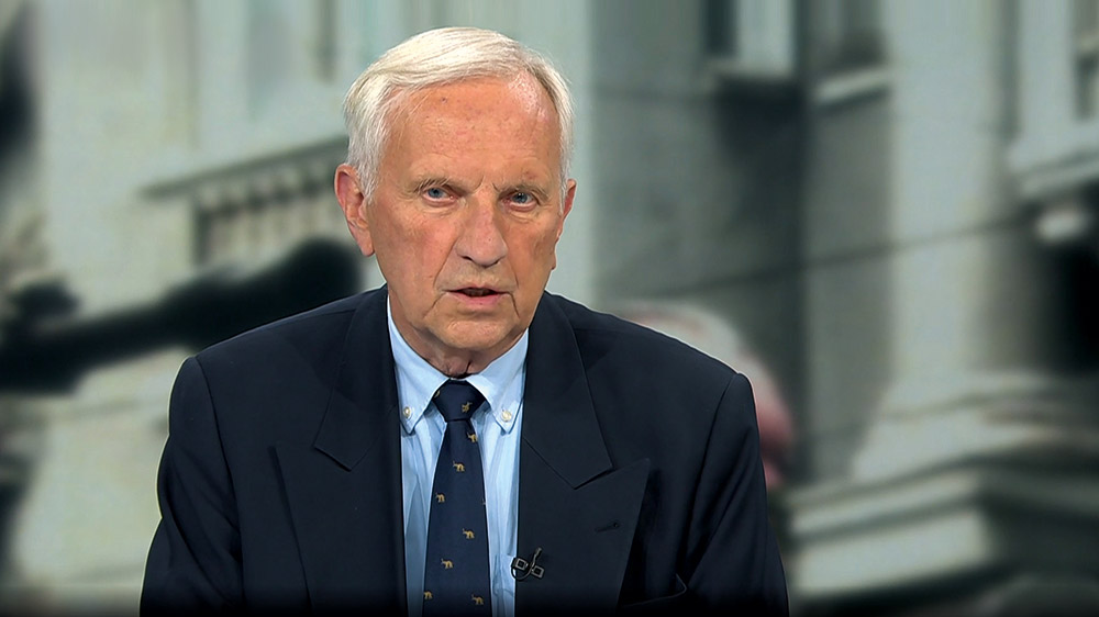 Älterer weißhaariger Mann im dunklen Anzug sitzt an einem Tisch