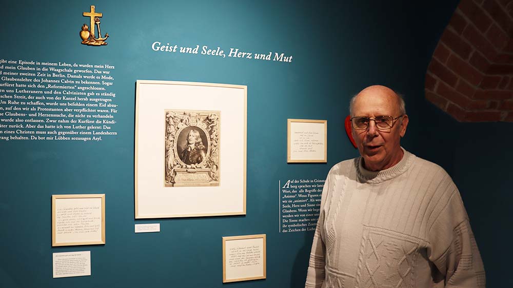 Ein Mann steht vor einer Wand mit Bildern und blickt in die Kamera